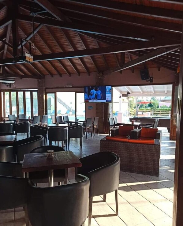 A restaurant with outdoor seating, a TV screen, and a pool view.
