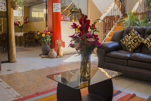 Un vestíbulo moderno con una mesa de centro de vidrio, un sofá de cuero con cojines estampados y un jarrón de flores sobre un piso de baldosas.