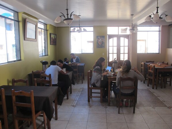 Un restaurante con mesas y sillas de madera, ventanas amplias y lámparas colgantes.