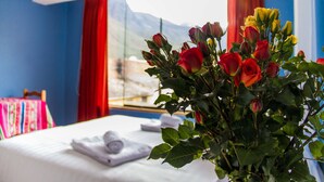 Een hotelkamer met een bed, een raam met uitzicht op de bergen en een roosbos op de nachtkastje.