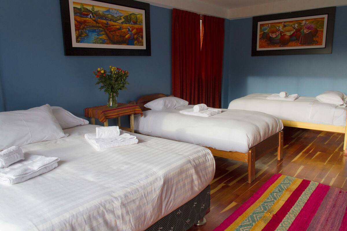 Habitación de hotel con dos camas, piso de madera y un tapete con rayas de colores.