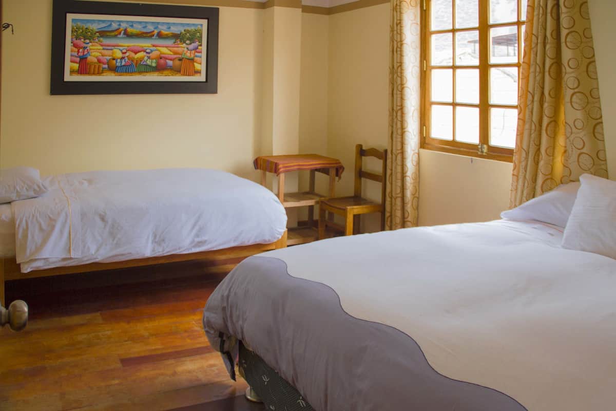 Habitación de hotel con dos camas, una silla de madera, una mesita y una ventana con cortinas.