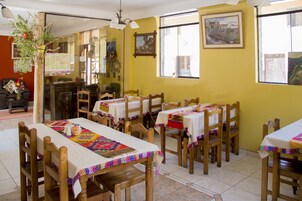 Un área de comedor con varias mesas y sillas, un ventilador de techo y un ventanal con vistas a edificios.
