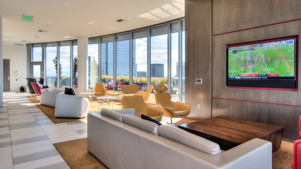 Un moderno espacio de descanso con asientos, una gran pantalla de televisión y amplias ventanas con vistas a la ciudad.