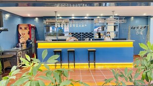 A bar area with a blue and yellow counter, stools, and a decorative metal rack.