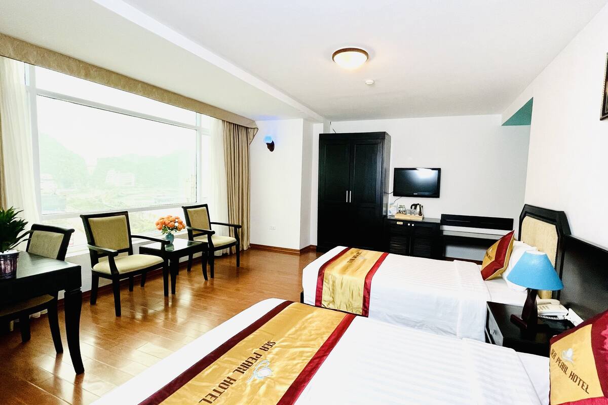 Habitació d'hotel amb dos llits, un escriptori amb cadira, televisió i finestra amb cortines.