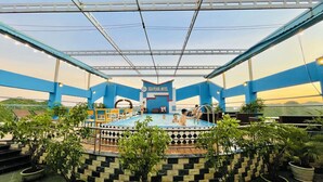 An indoor swimming pool with a blue and white color scheme, surrounded by potted plants and a checkered floor pattern.