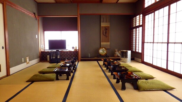 A tatami mat room with a television, tatami mats, cushions, and a traditional Japanese aesthetic. - Okubo Ryokan (Komatsu)