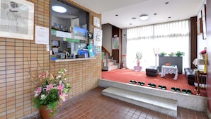 A reception area with a tiled wall, a reception desk, a staircase, and a seating area with a table and chairs. - Okubo Ryokan (Komatsu)