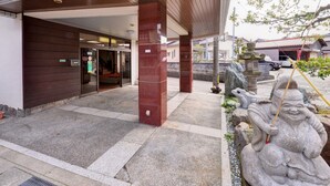 A building entrance with a tiled roof, a wooden facade, and a stone pathway leading to a traditional stone lantern. - Okubo Ryokan (Komatsu)