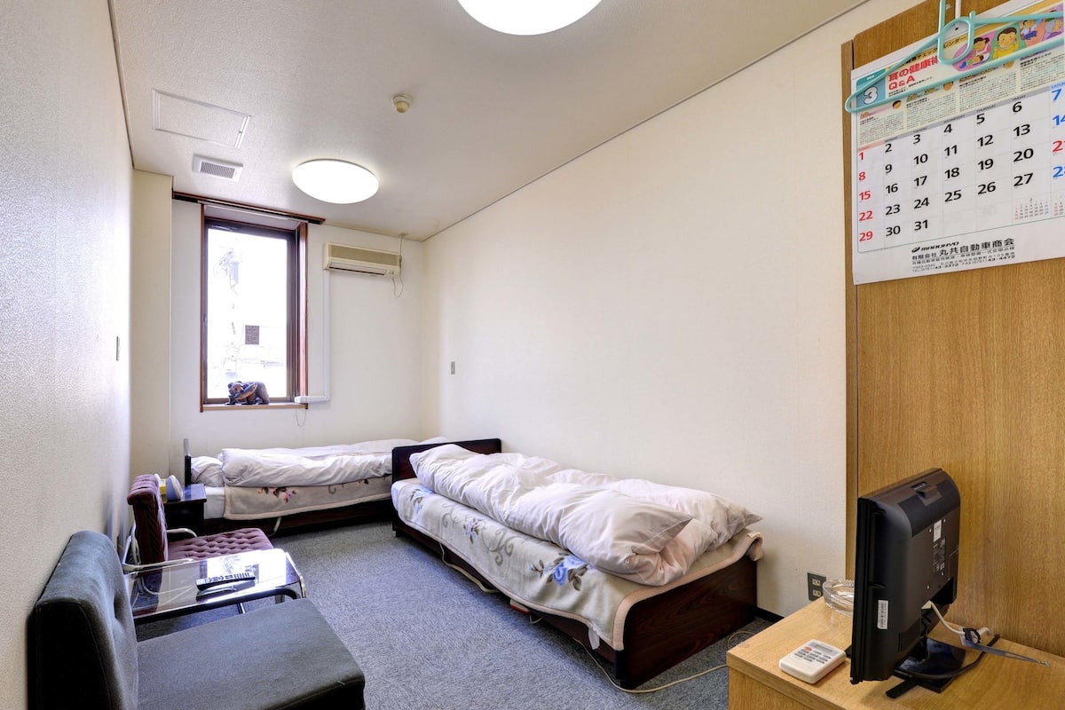 Una habitación de hotel pequeña con dos camas individuales, un escritorio con una computadora, una silla y un calendario en la pared.