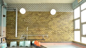 A swimming pool area with a tiled floor, a brick wall, and a window. - Okubo Ryokan (Komatsu)