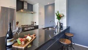 A modern kitchen with a stainless steel refrigerator, a wine bottle, and a cutting board with fruits and cheese. - Villa Two at Vailmont Queenstown (Queenstown)