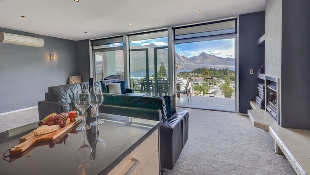 A modern living room with a glass dining table, a sofa, and a view of mountains and a lake. - Villa Two at Vailmont Queenstown (Queenstown)