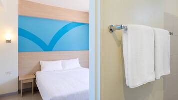 A hotel room with a bed, a nightstand, a wall with a blue design, and a towel rack with two towels.