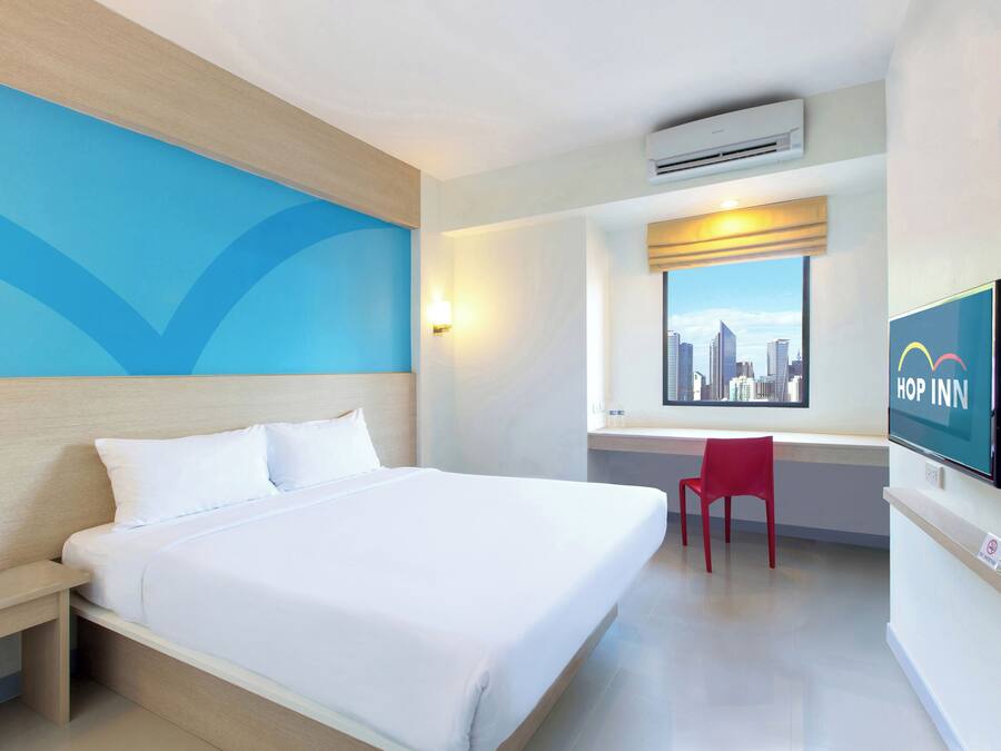 Ein Hotelzimmer mit Bett, Schreibtisch, Stuhl, Fernseher und einem Fenster mit Blick auf die Stadt.