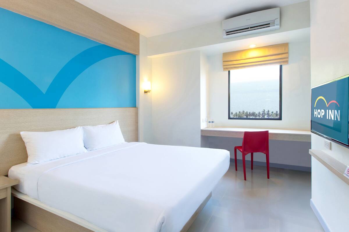 A hotel room with a bed, a desk, a chair, a TV, and a window with a view.
