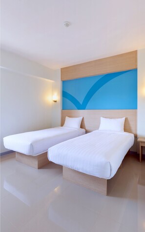 Quarto de hotel com duas camas de solteiro, cabeceira de madeira, parede azul decorativa e mesa de cabeceira com abajur.