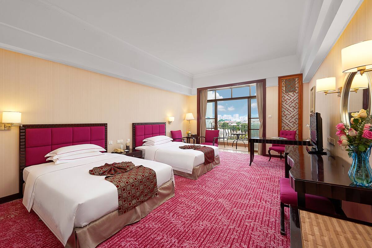 A hotel room with two beds, a desk, and a balcony with a view.