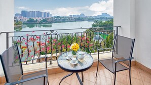 A balcony with a table set for tea, chairs, and a view of a cityscape and lake.