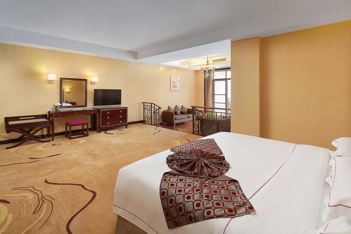 A hotel room with a large bed, a desk with a television, a small table, and a sofa.