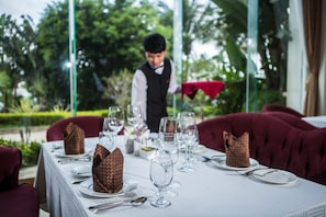 A dining table set with white tablecloth, plates, and cutlery, with a waiter in the background.