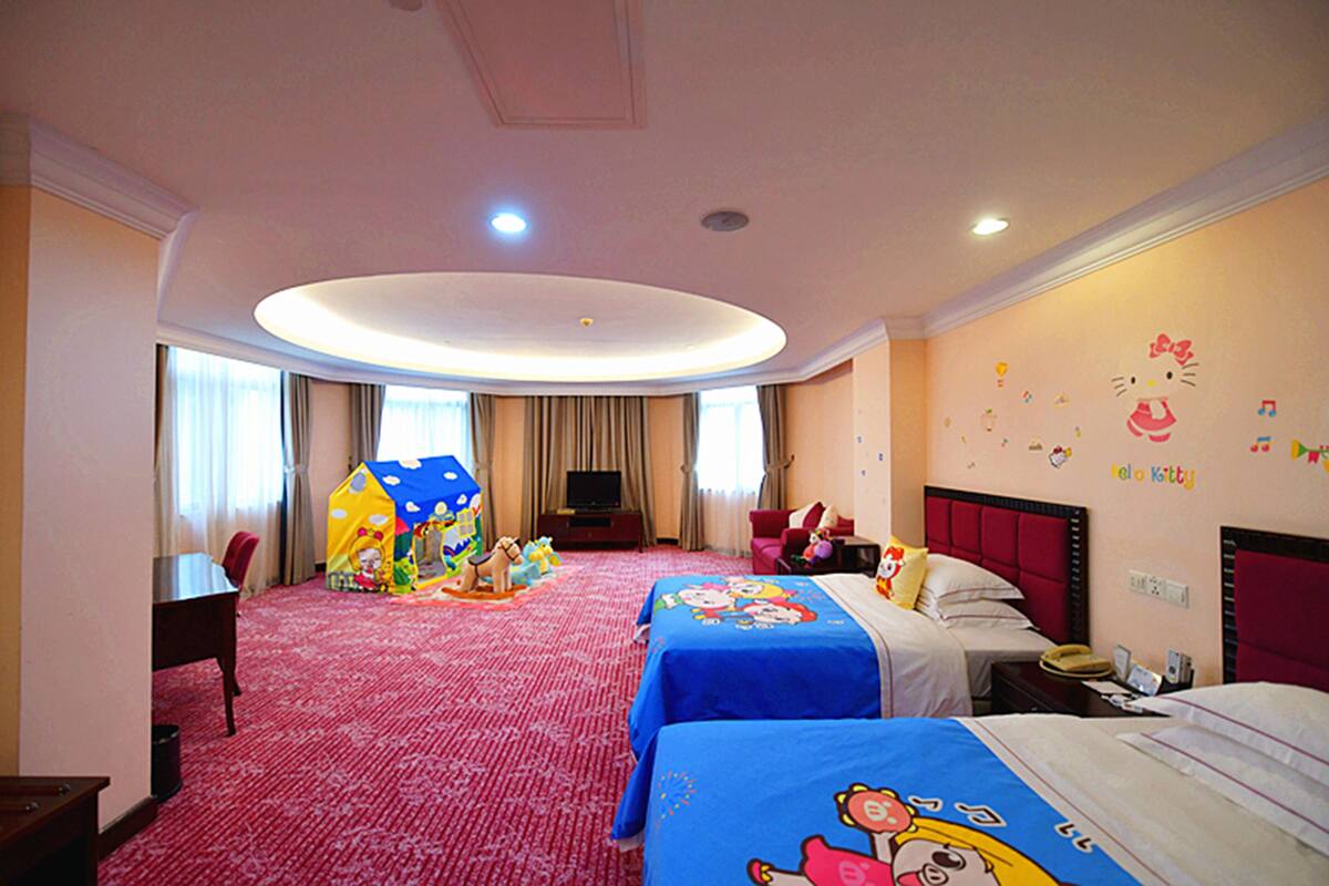 A hotel room with two beds, a play area, a TV, and a red headboard.