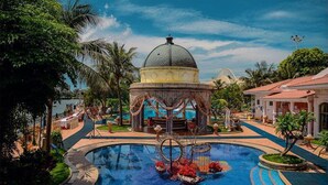 A pool area with a central fountain, surrounded by palm trees and a gazebo.