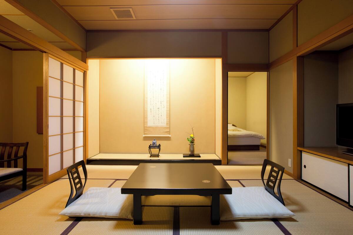 A traditional Japanese room with tatami flooring, a low table with cushions, a TV, and sliding doors.