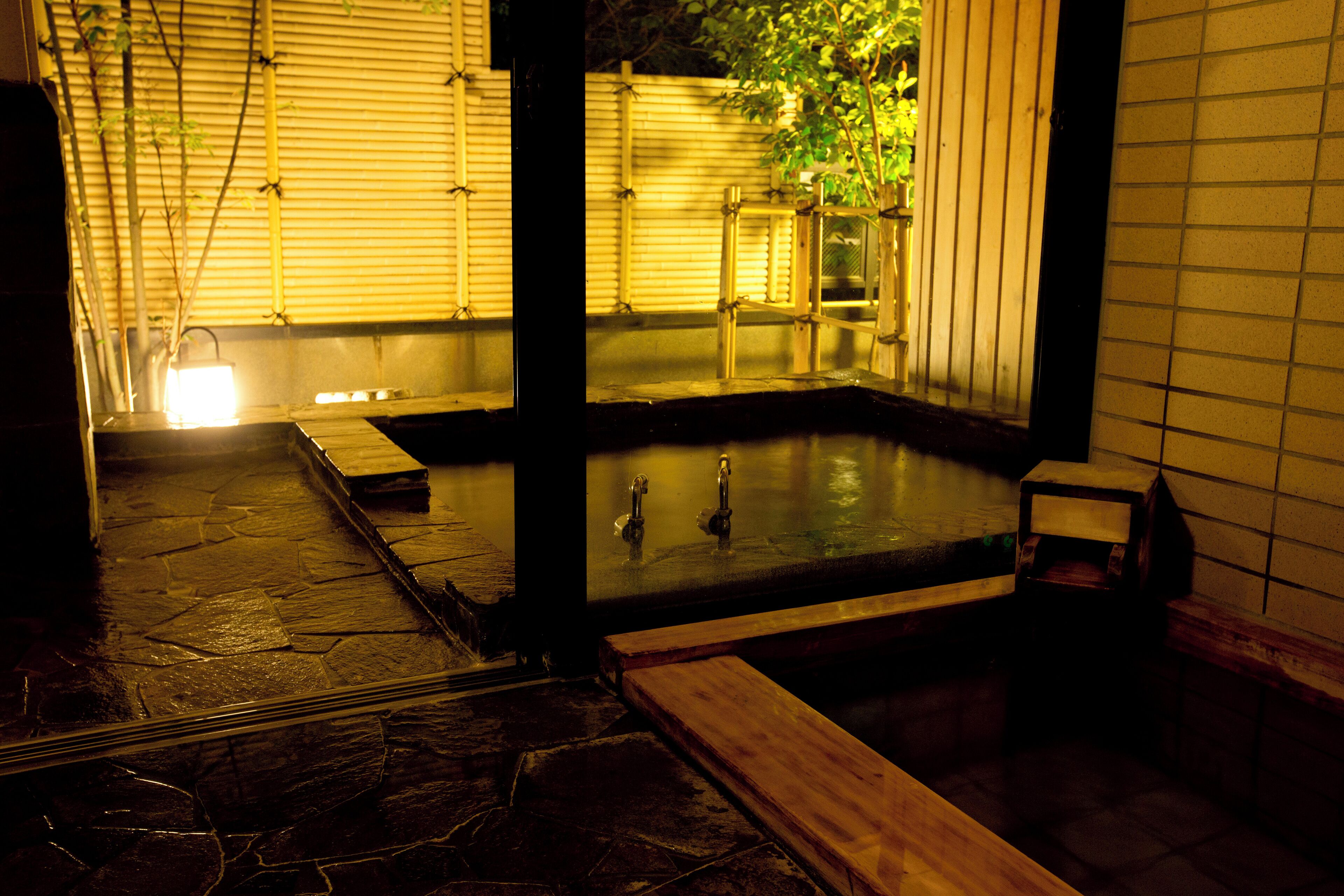 A traditional Japanese onsen with a stone floor, wooden benches, and a small wooden structure.