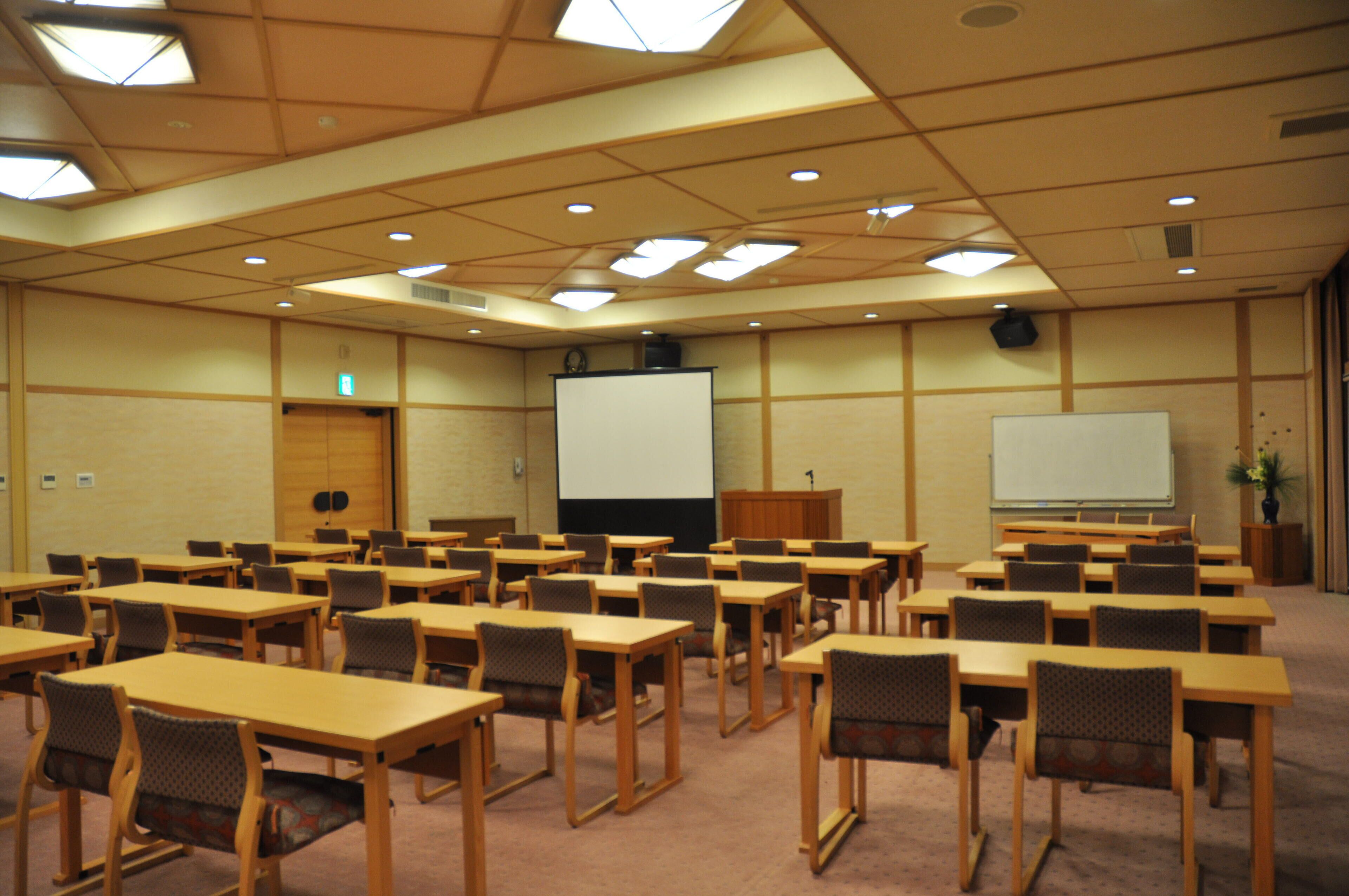 Una sala de conferencias con varias mesas y sillas, una pantalla de proyector y una pizarra.