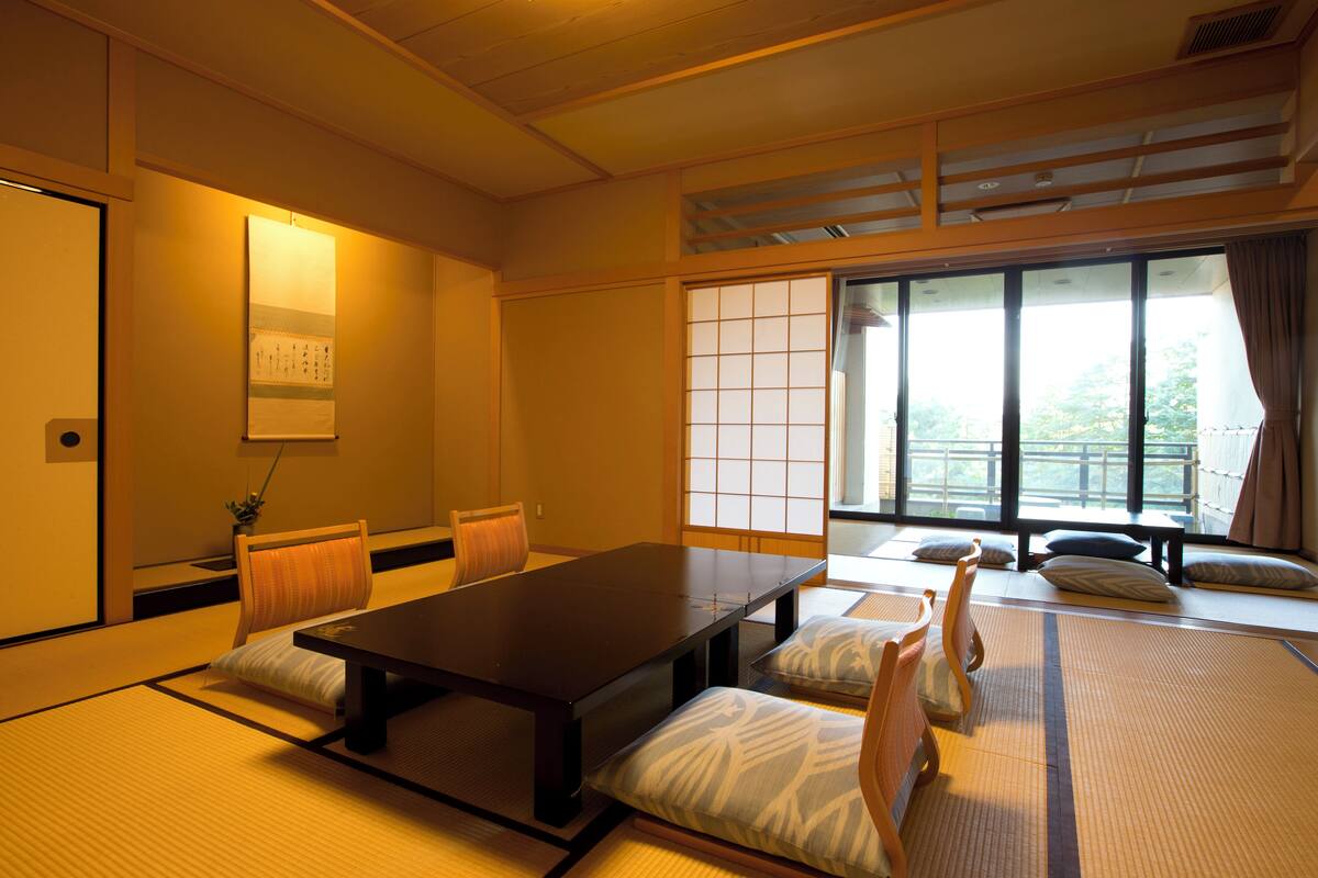 A traditional Japanese room with tatami flooring, a low table, cushions, and sliding shoji doors.