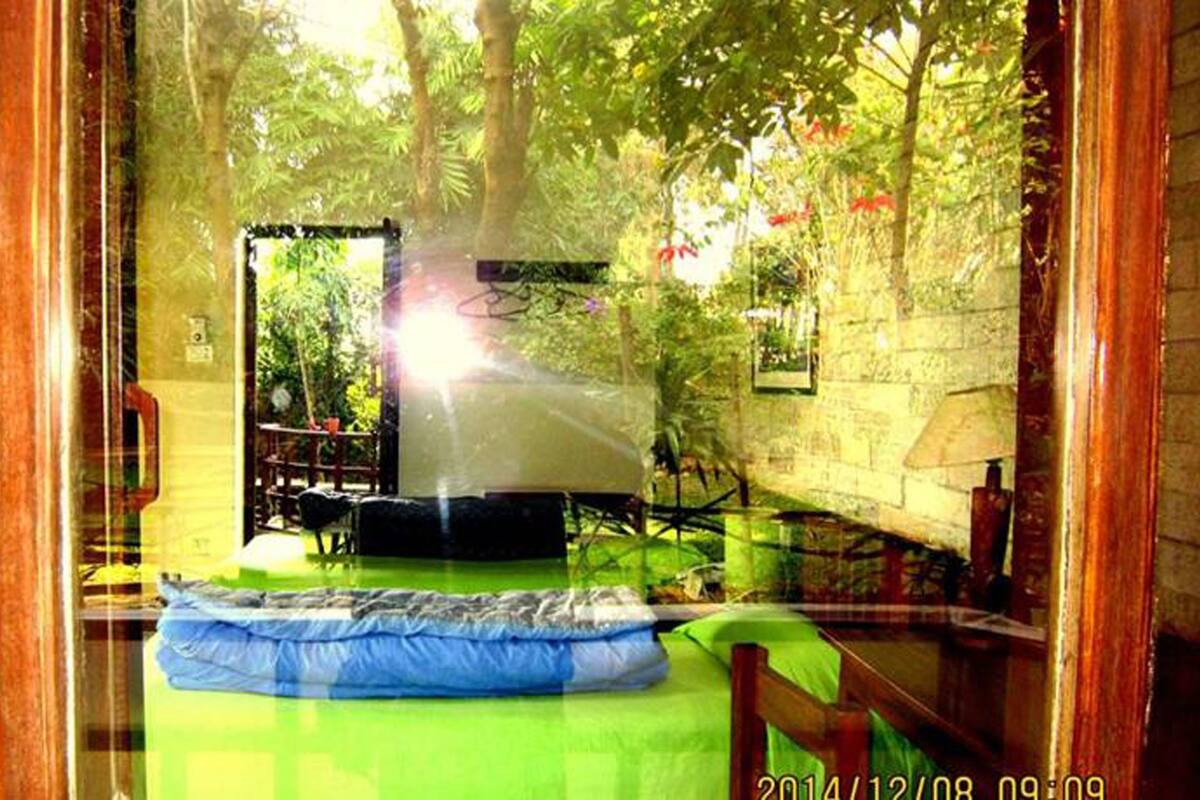 A room with a bed, a chair, a table, and a window overlooking a garden.