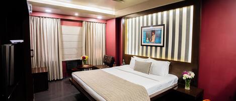 A hotel room with a large bed, a desk, a chair, a ceiling fan, and a window with curtains.