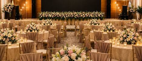 A banquet hall with round tables, chairs, floral centerpieces, and recessed lighting.