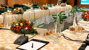A conference room with tables set for a meeting, equipped with microphones, nameplates, and floral centerpieces.