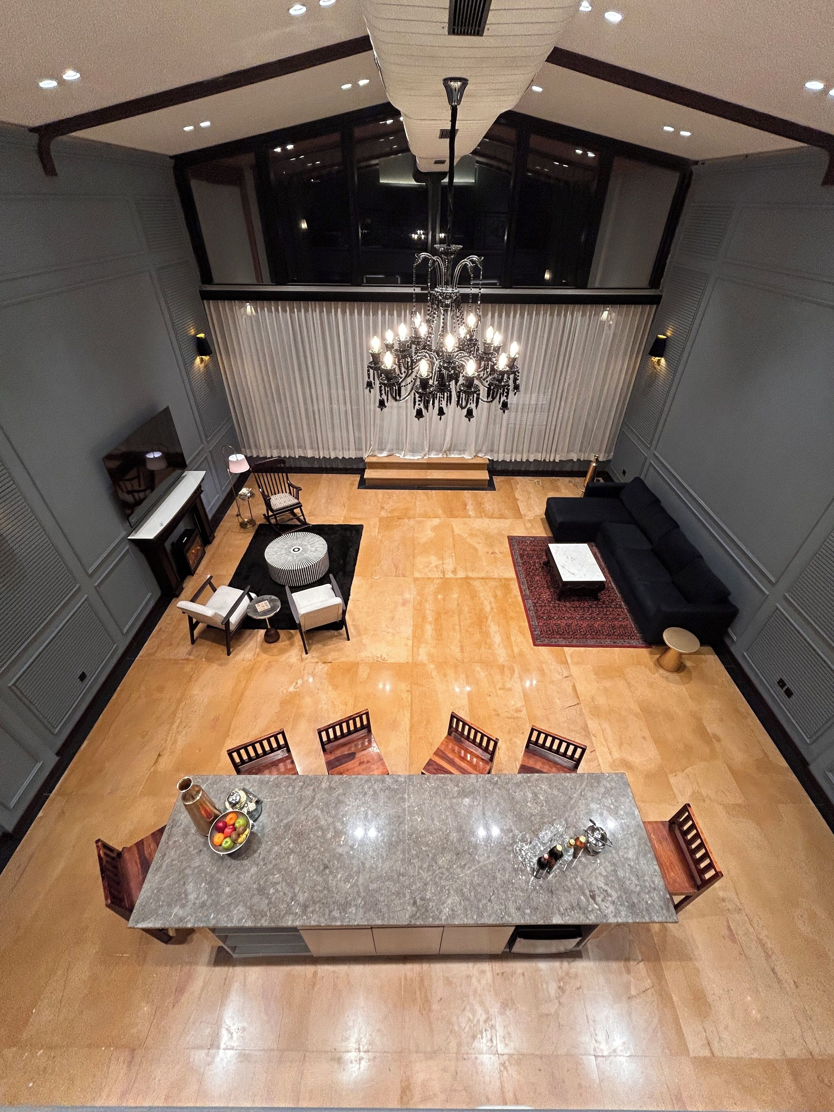 A spacious living area with a large chandelier, a dining table, and a seating arrangement.