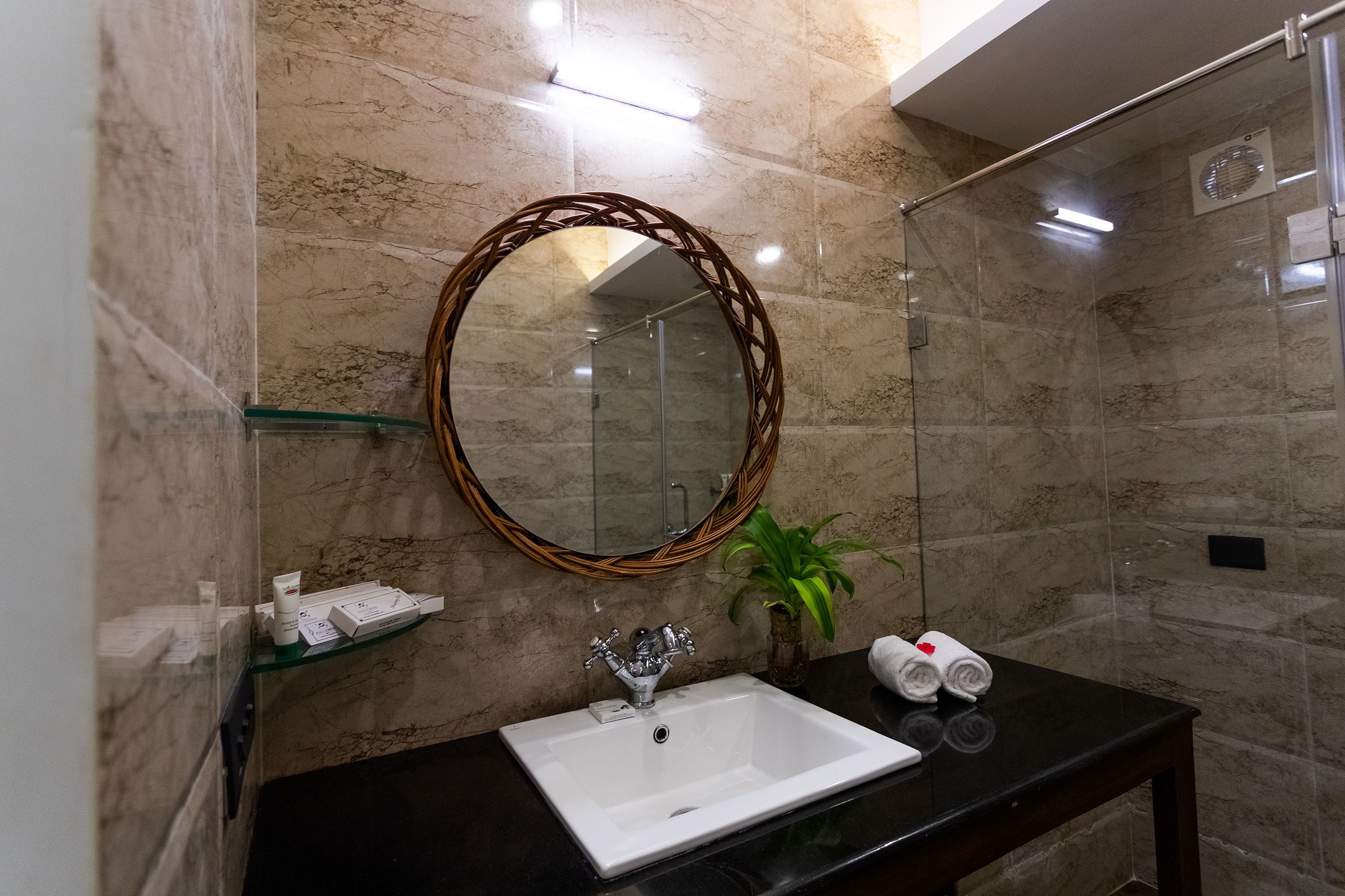 Un bagno con un lavandino bianco, uno specchio con cornice in vimini e una pianta in vaso.