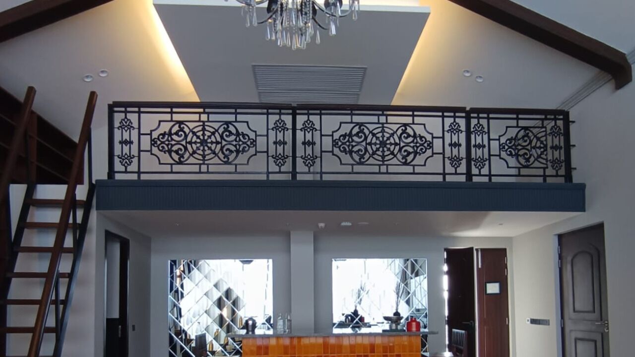 A spacious room with a balcony, a chandelier, and a kitchen area visible through the windows.