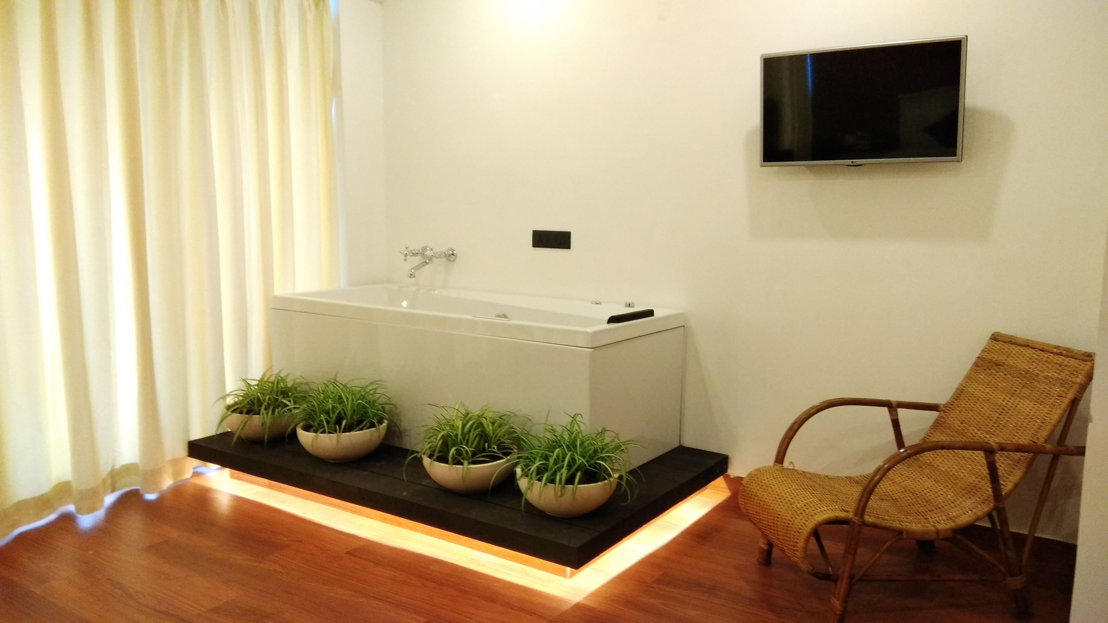 A modern bathroom with a bathtub, a flat-screen TV, and a wicker chair.