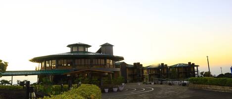 A large, modern building with a curved roof and multiple levels, surrounded by landscaped gardens and a parking area.