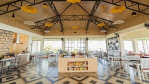 A spacious indoor area with a high ceiling, wooden beams, and multiple hanging yellow and white umbrellas. There is a central island with shelves displaying various items, surrounded by white chairs and tables. -  Polo Cherrapunjee Resort  (Shillong)