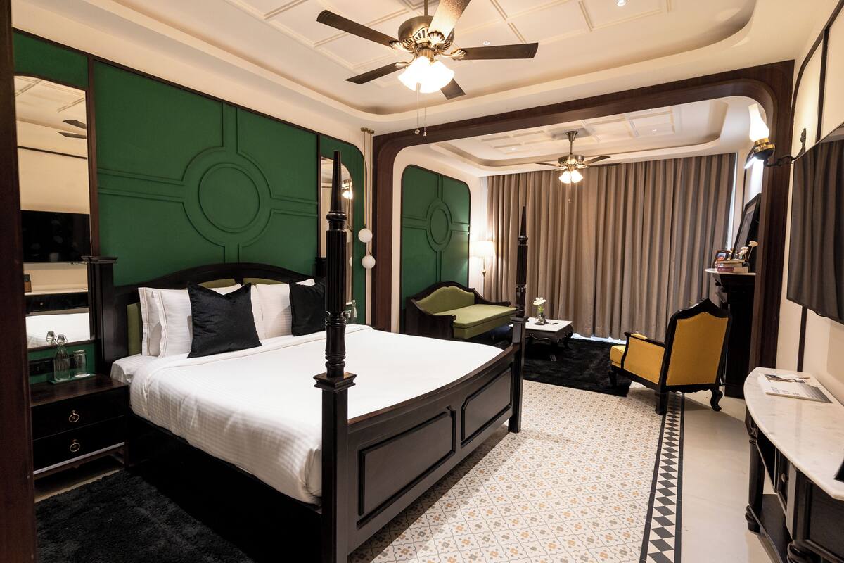 Ein Hotelzimmer mit einem großen Bett, einem Schreibtisch, einem Stuhl, einem Deckenventilator und einem großen Fenster mit Vorhängen.