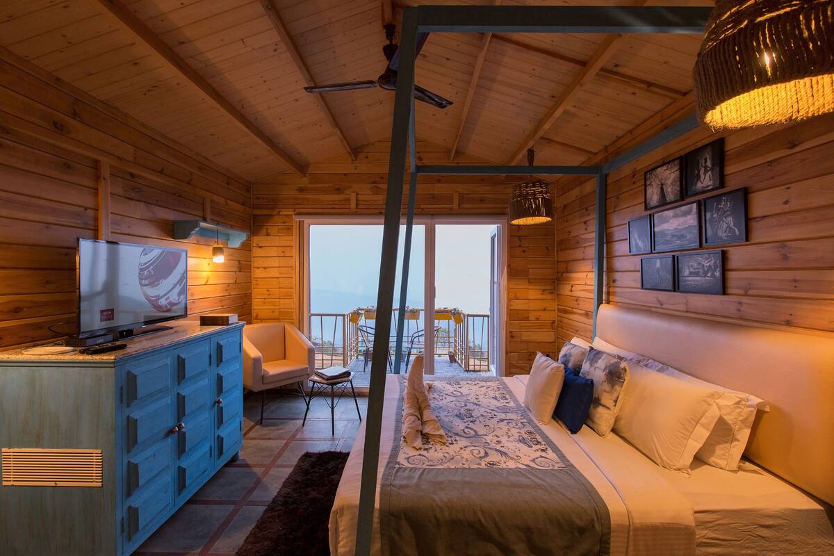 Ein Holzblockhaus-Innenraum mit Bett, Fernseher, Schreibtisch und einem Balkon mit Aussicht.