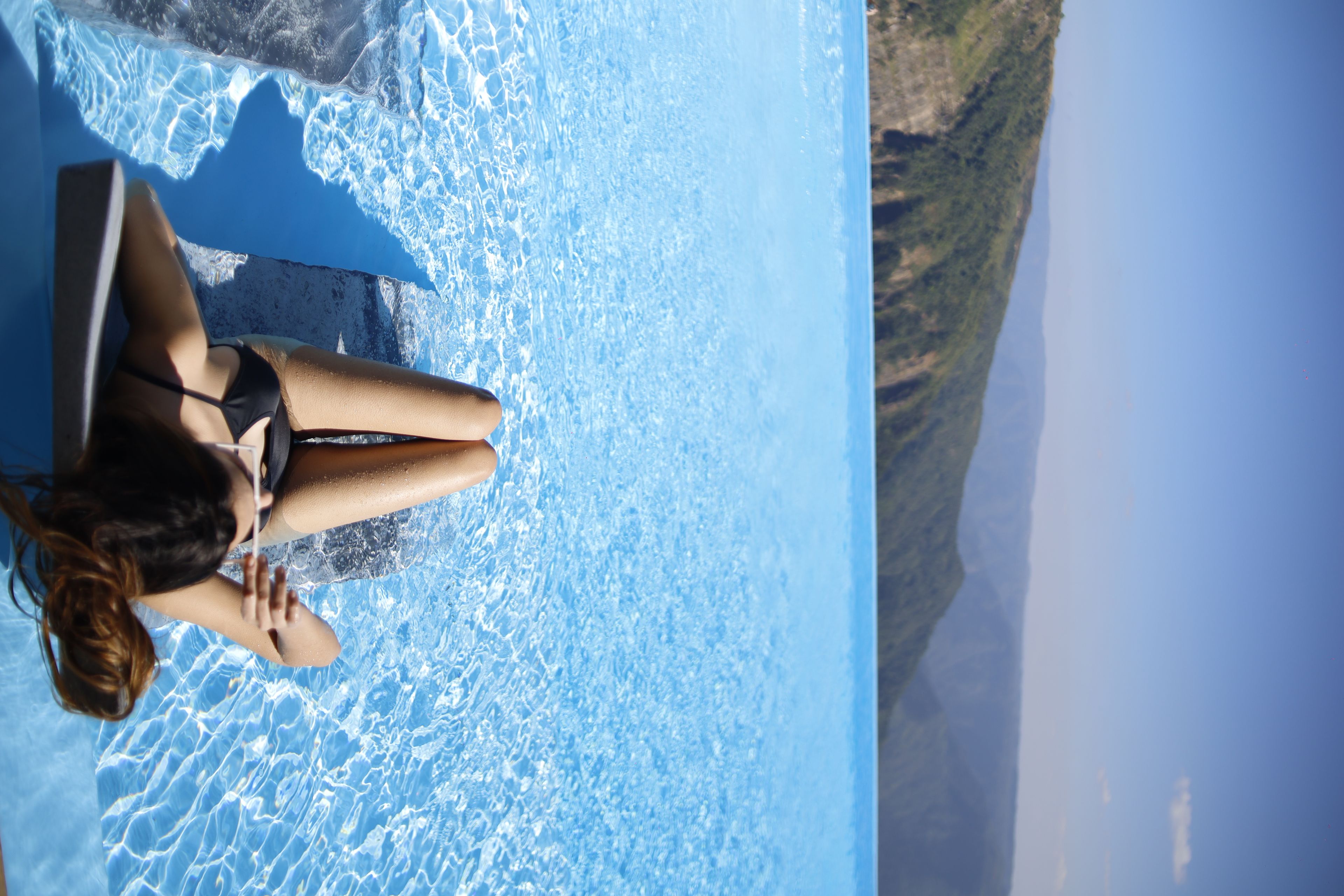 Eine Frau sitzt am Pool mit freiem Blick auf die umliegende Landschaft.