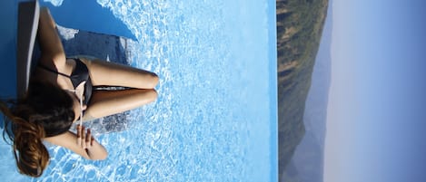 A woman sitting by a pool with a clear view of the surrounding landscape.