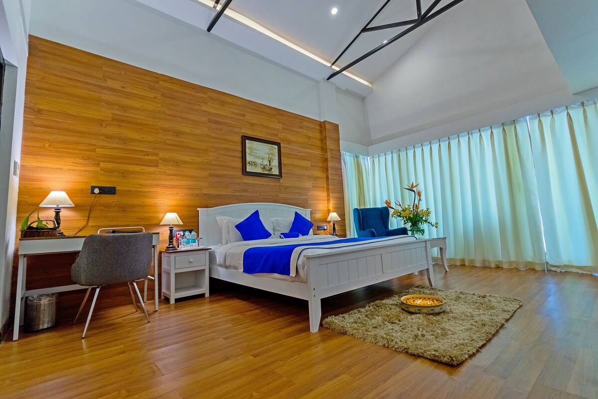 Ein modernes Schlafzimmer mit einer Wand in Holzoptik, einem Bett mit blauer Bettwäsche, einem Schreibtisch mit Stuhl, einem Nachttisch und einer dekorativen Schale auf einem Teppich.