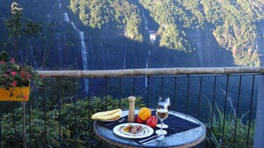 A table with a meal and a glass of wine, overlooking a waterfall and lush greenery. -  Polo Cherrapunjee Resort  (Shillong)