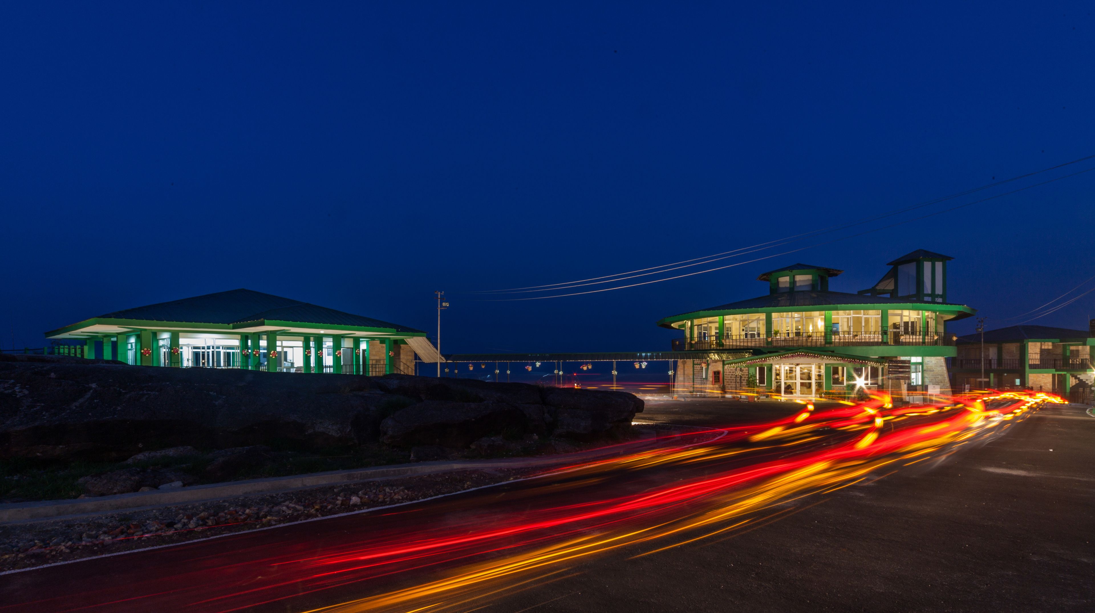 A brightly lit building with a green roof and a separate tower structure, connected by a bridge.
