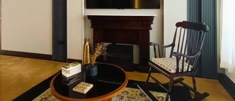A living room with a fireplace, a television, a rocking chair, and a coffee table with decorative items.
